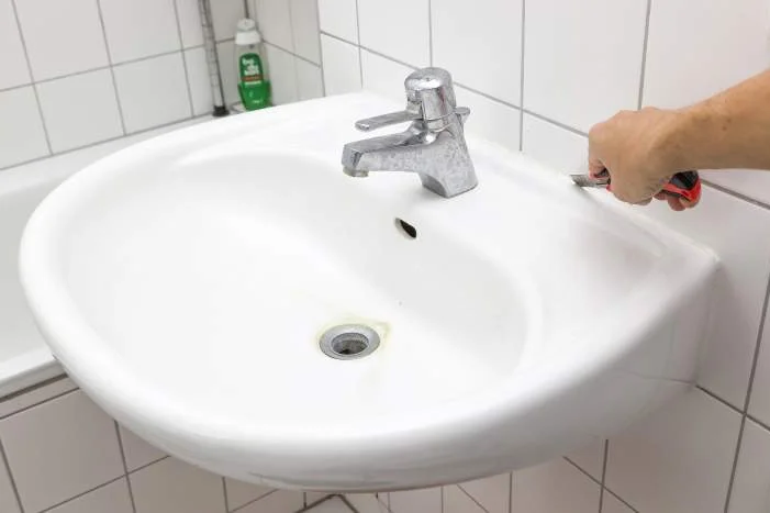 Person entfernt Silikonfuge an Waschbecken mit Cuttermesser